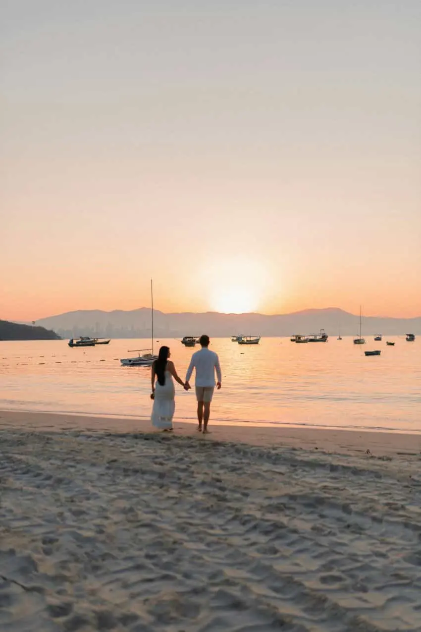 A couple holding hands while walking along a sandy beach at sunset depicting a sense of love and romance